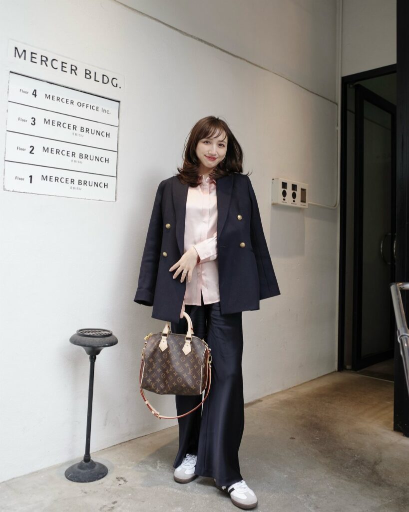 Woman wearing a navy blazer, pink shirt, and navy wide-leg trousers with white sneakers.