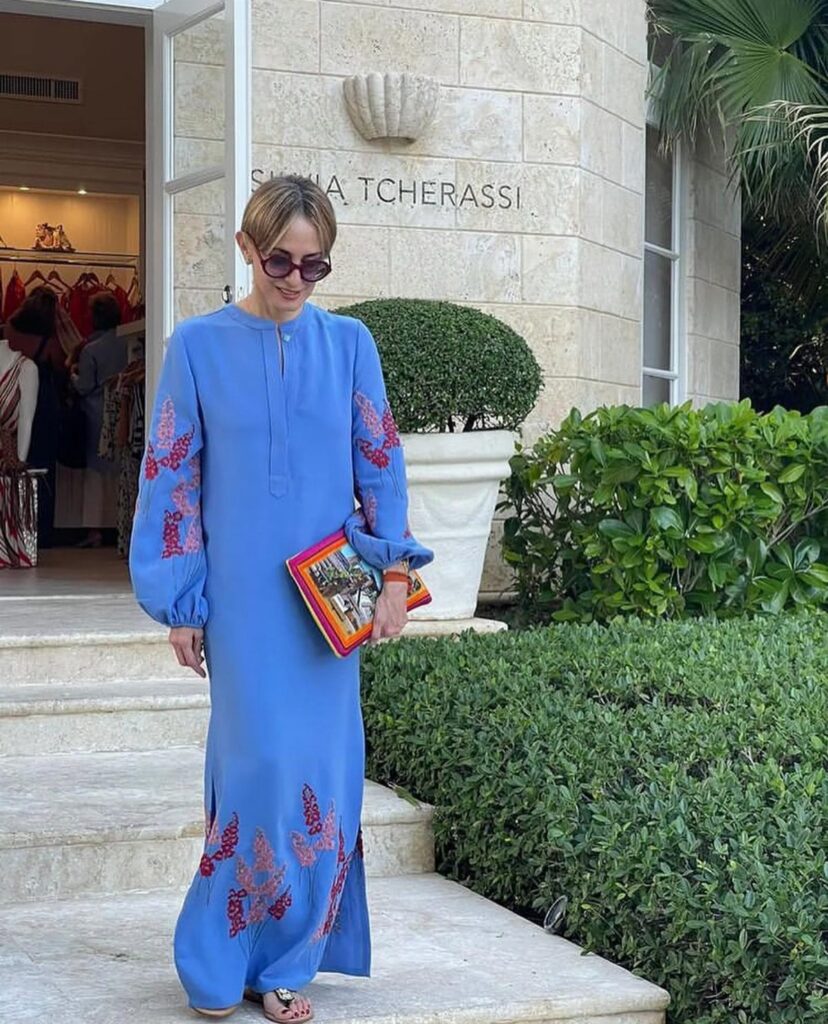 A woman in a blue embroidered maxi dress walking down stone steps outside a building.