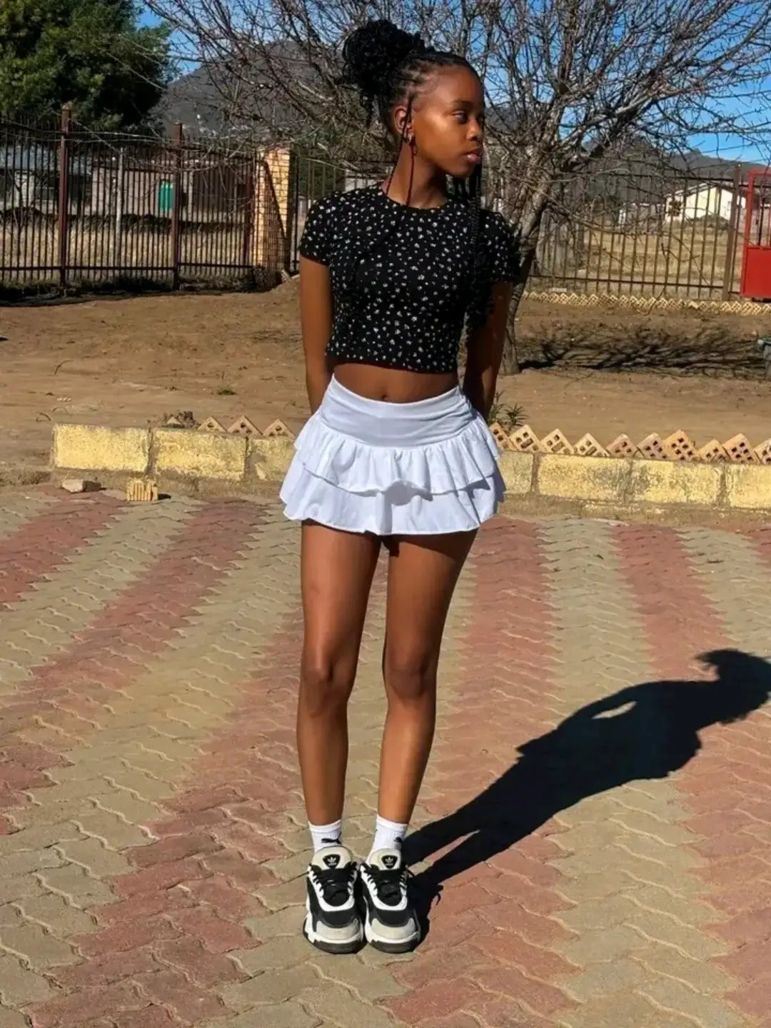 A young woman posing in a black polka-dot crop top and white ruffled skirt.
