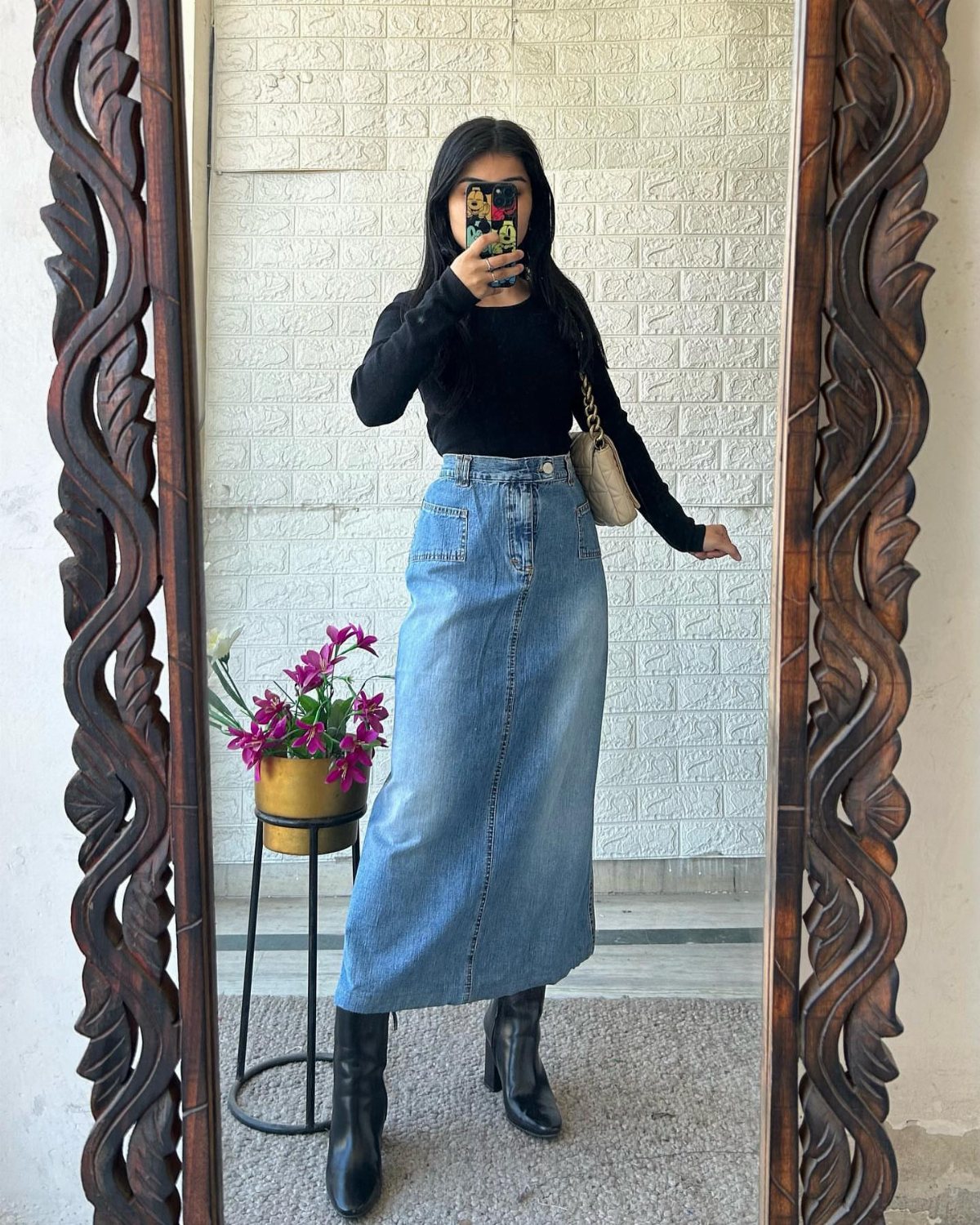 A woman posing in a long denim maxi skirt and black top for a mirror selfie.