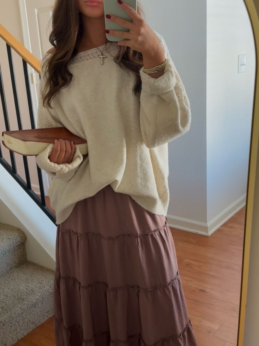 Woman in a cream sweater and mauve tiered skirt posing for a mirror selfie.