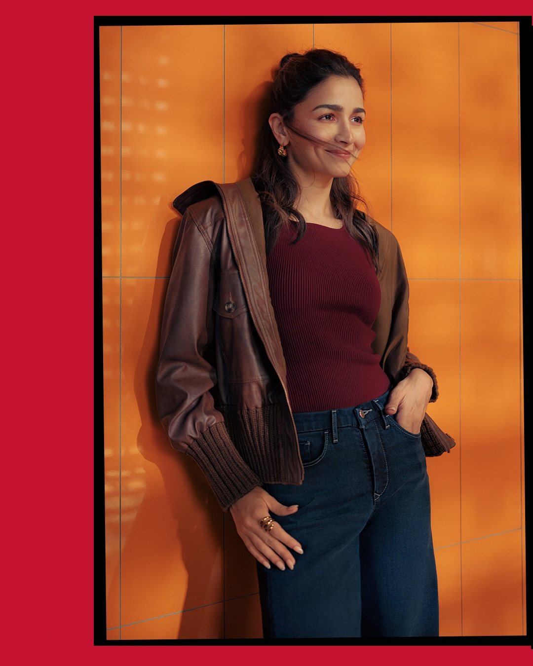 A woman smiling while wearing a brown leather bomber jacket, burgundy top, and blue jeans.