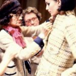 An older woman adjusting a cream tweed jacket on a younger woman.