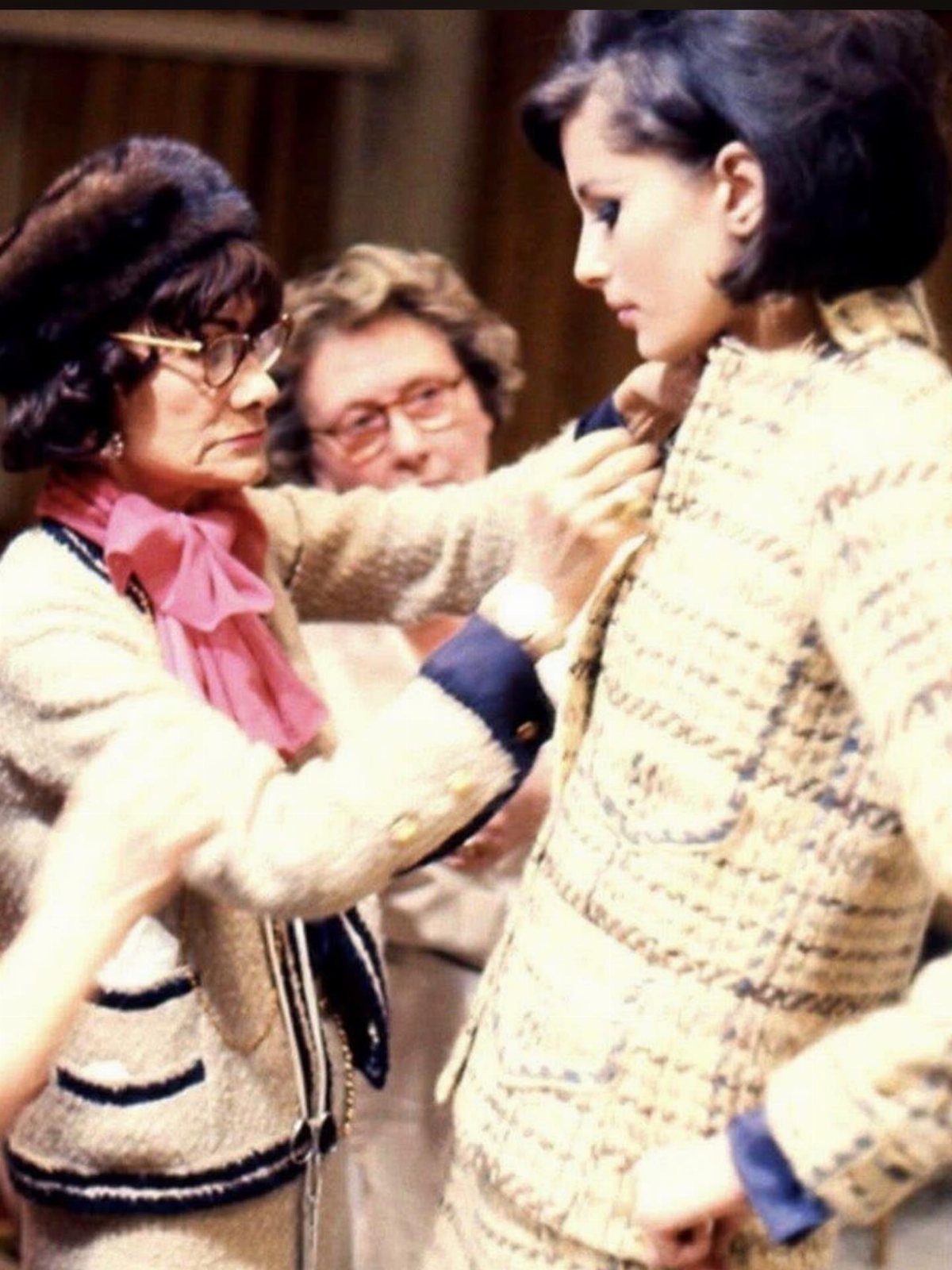An older woman adjusting a cream tweed jacket on a younger woman.