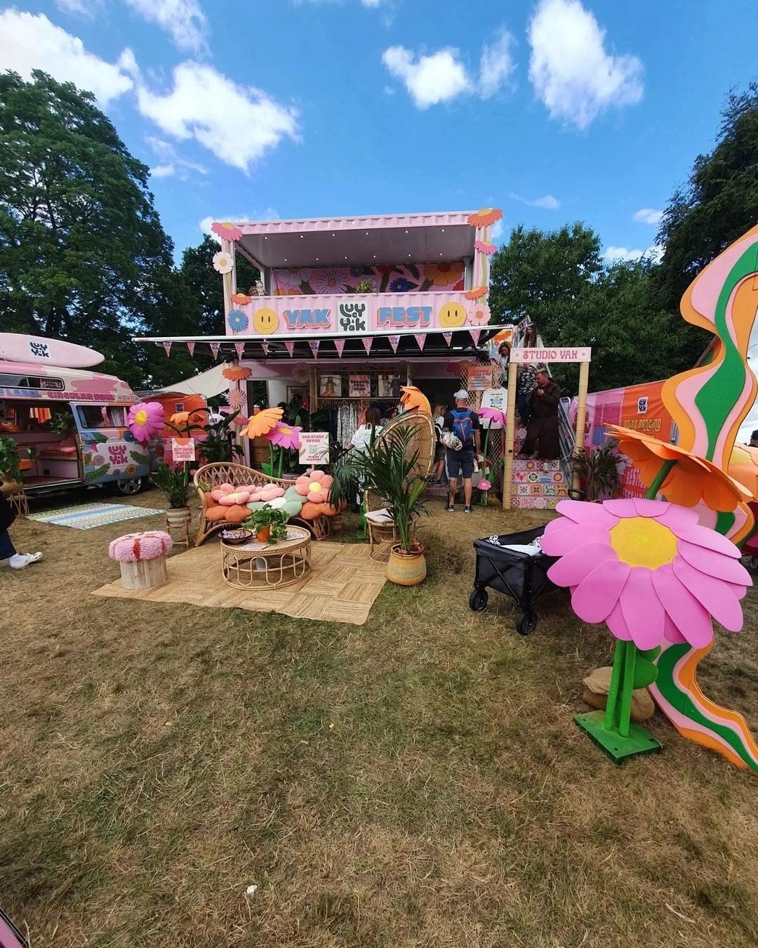 A vibrant pink festival pop-up installation with large flowers and lounge seating on a grassy field.