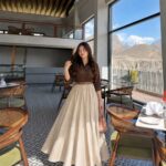 Woman posing in a brown shirt and cream high-waisted maxi skirt inside a cafe.