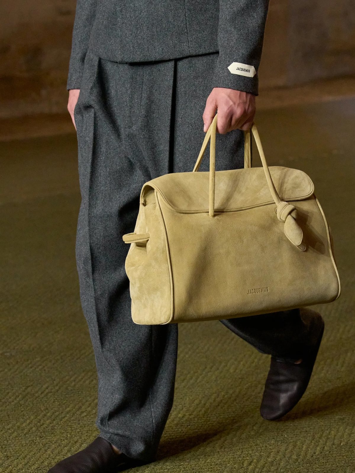 A person walking while carrying a large, light yellow suede handbag with two handles.