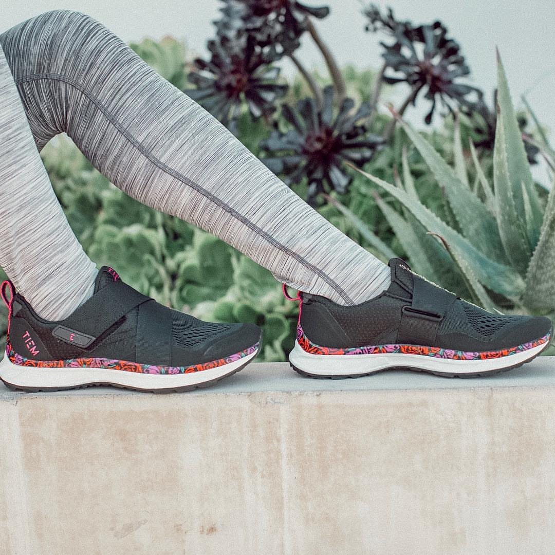 Black athletic sneakers with patterned soles worn by a person in grey leggings.