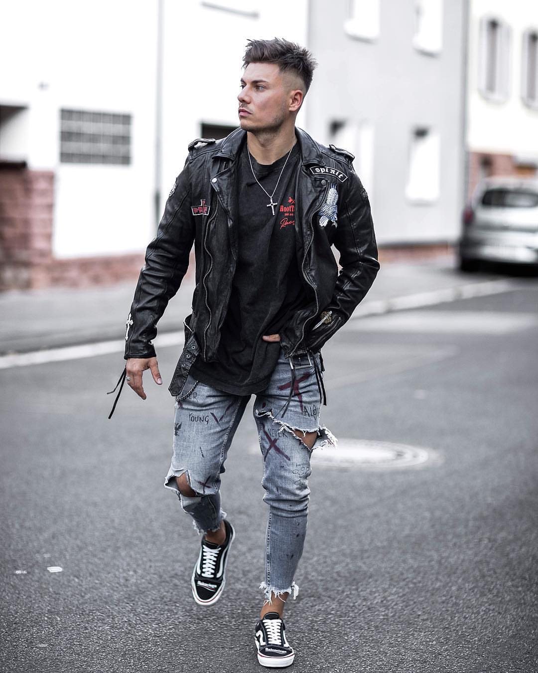 Man walking down a city street wearing a black leather jacket and ripped blue jeans.