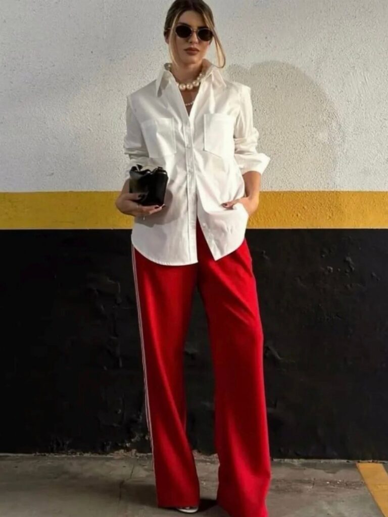 Woman posing in a white shirt and wide-leg red trousers with white stripes.