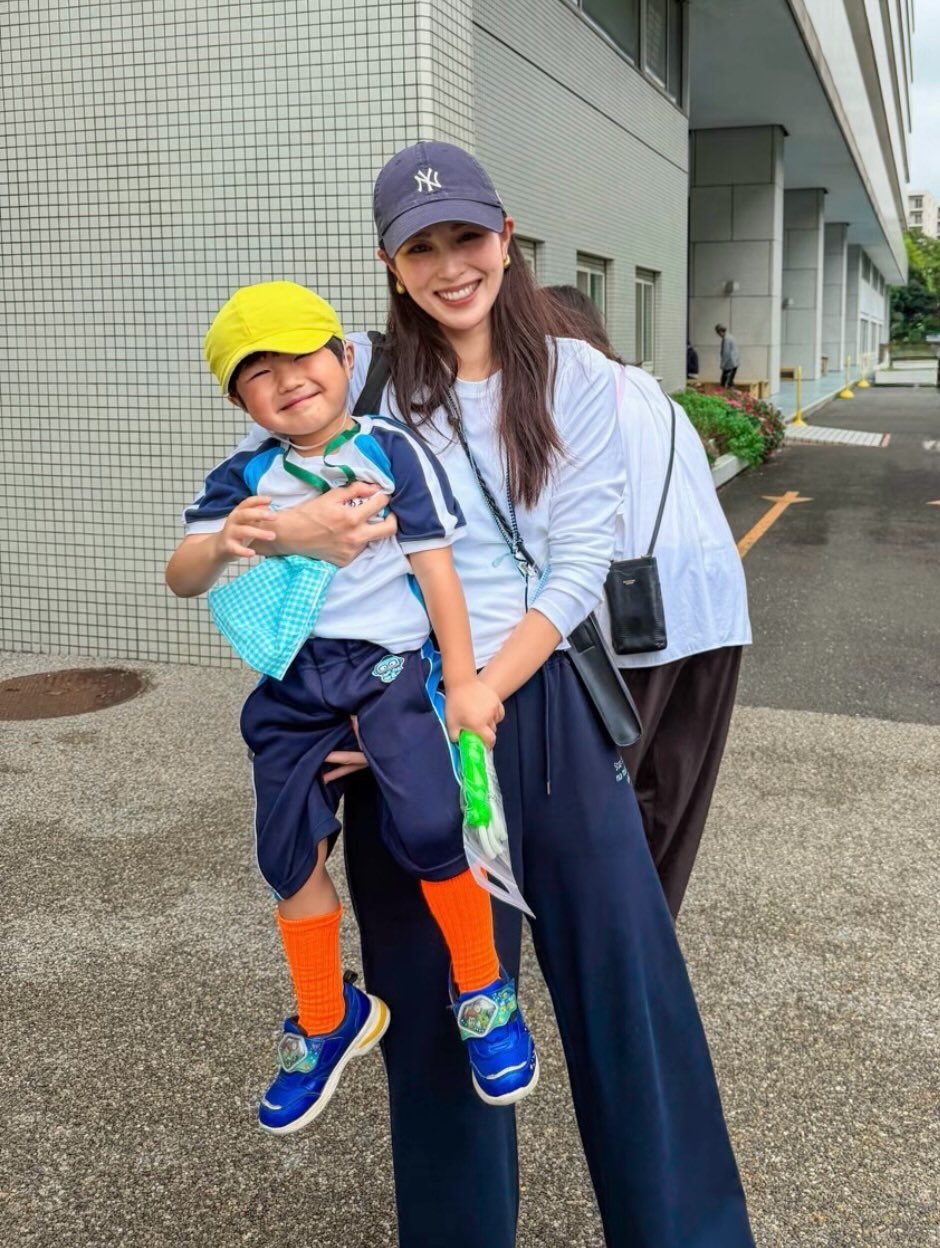 A woman in a white shirt and navy joggers holding a young boy in athletic wear.