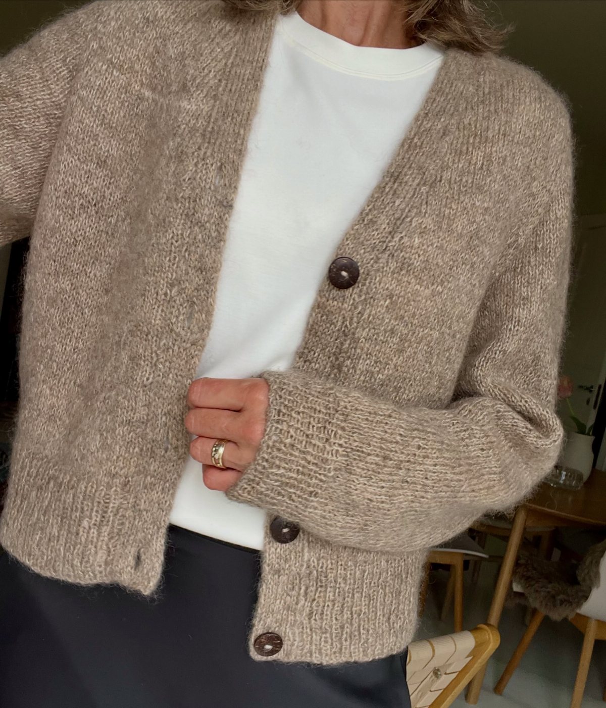 A person wearing a fuzzy light brown knit cardigan over a white t-shirt.