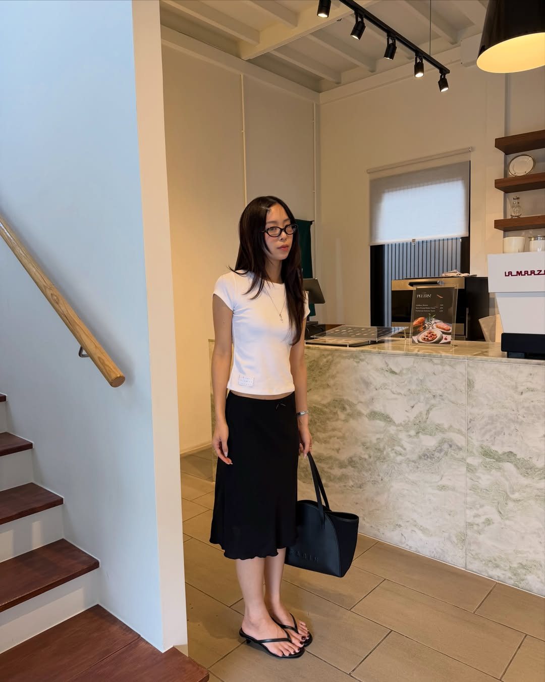 Woman standing in a room wearing a white t-shirt and a black midi skirt.