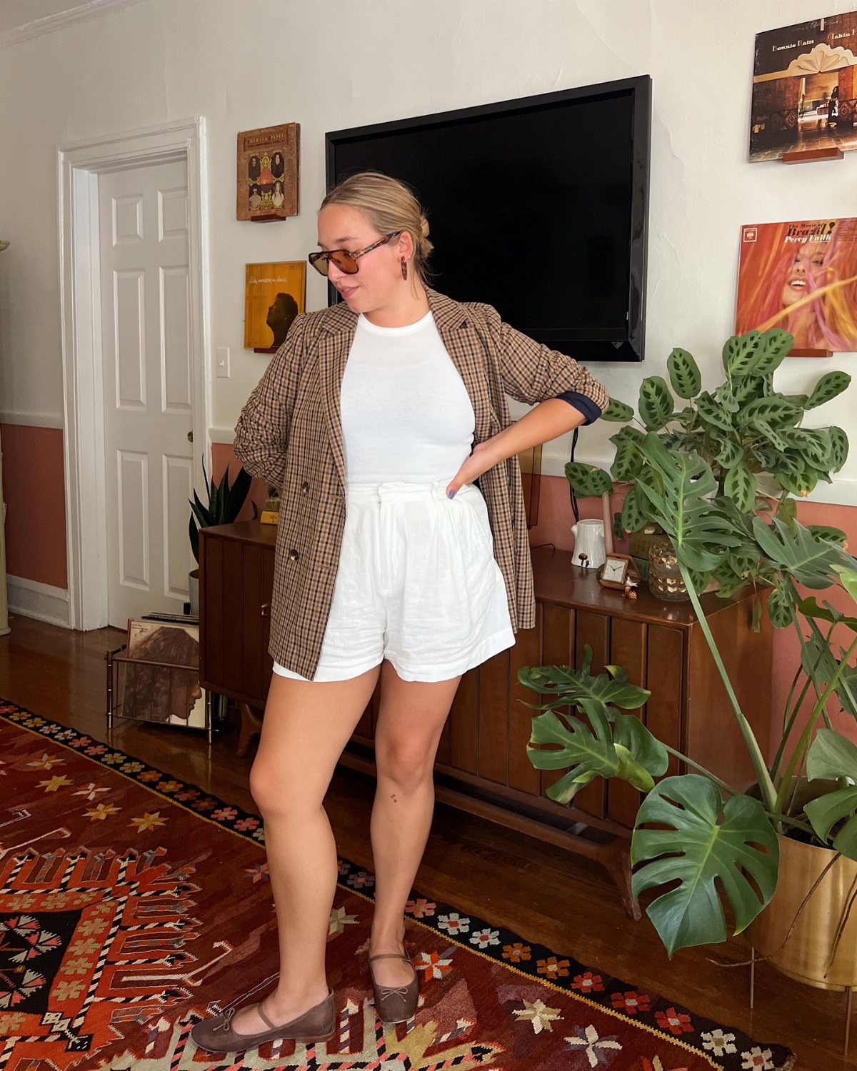 Woman posing in a white t-shirt, white shorts, and a patterned oversized blazer indoors.